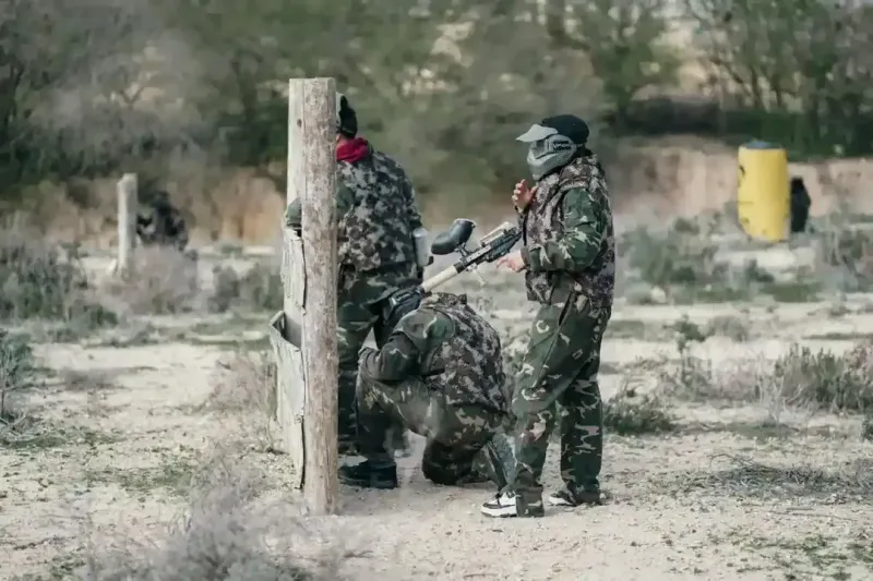 Skupina lidí v maskáčích hrající paintball nebo airsoft v lese